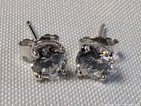 Close-up view of pair of sterling silver stud earrings with round clear stones, showing four-prong setting and butterfly backings.