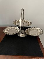 Front view of the 3 tiered vintage silver-tone metal serving stand showing three scalloped edge trays and carrying handle.
