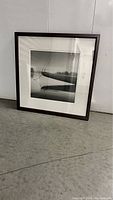 Framed and matted black and white photo of a sailboat leaning against a gray wall, showing the overall front view of the item.