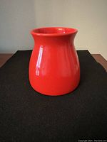 Photo of a red ceramic vase placed on a dark cloth, showing its shape and glossy red finish.