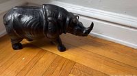 Front and side view of the black leather decorative rhino statue positioned on wooden flooring near a white baseboard.