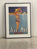 Framed vintage poster showing woman in beachwear with coastal background and text 'Juan les Pins Antibes'. Black frame with white matting.