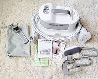 Rowenta IS1430 Pro Compact steamer with hose, fabric brush attachments, protective glove, hanger clips, storage pouch, and manuals arranged on a carpet.