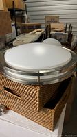Photo of round flush mount ceiling light showing silver trim and frosted white diffuser on a woven basket.