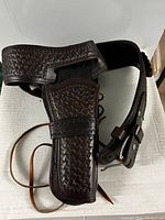 Dark brown leather belt with attached holster showing basket weave embossing and leather lacing detail.