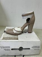 Side profile of one beige Aldo Vezna heel showing pointed toe and block heel, positioned on top of worn shoebox.