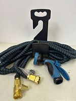 Photo of the expandable garden hose coiled with the blue and black spray nozzle and two brass fittings attached in front. Items are arranged on a flat surface against a white background.
