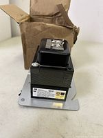 Hammond BF2F Transformer mounted on a metal baseplate with terminal connectors visible on top. Transformer placed beside its original brown cardboard box which has minor damage.