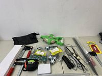Overview of various hand tools including clamps, measuring tape, gloves, and measuring wheel arranged on a tabletop