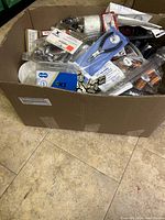 Photo showing assorted items in box including chain links, scissors, a bicycle chain, and packaged batteries.
