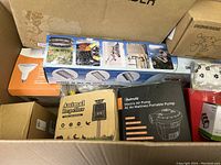 Box containing multiple boxed items including a keyboard holder, animal repeller, electric air pump, and others.