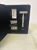 Open box showing matte stainless steel adjustable razor handle with two interchangeable razor head plates and Rockwell blade pack