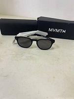 Front angle view of MVMT Hyde sunglasses in front of black MVMT box and case
