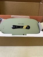 Green My OBI heated eye massager in original box, showing front control panel and charging port.