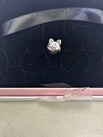 Close-up photo of Pandora curious cat charm resting in a black velvet jewelry holder inside a pink box showing the charm's cat face detail.