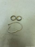 Photo showing two men's sterling silver rings and a small sterling silver ankle bracelet on a plain background.