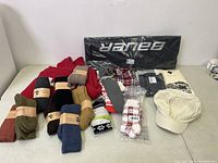 View of assorted wool socks, hats, scarves and a cream-colored cap, plus a black Baum branded item still in packaging.