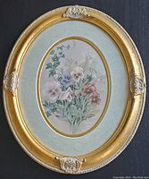 Full view of the framed floral print showing the overall oval shape, decorative gold frame with silver accents, and the floral image highlighted against the oval mat.