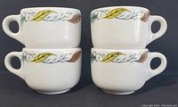 Four white ceramic coffee mugs stacked in two pairs, showing the same leaf pattern decoration on the upper rim with yellow, brown, and green colors.