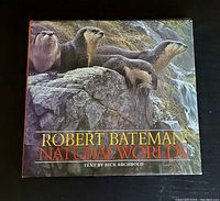 Front cover of the hardcover book showing three otters on a rocky background with water, titled 'Robert Bateman Natural Worlds'