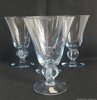 Four clear crystal Skruf Blue Gulli Ingrid cocktail glasses with bubble detail on stem and original labels on base, arranged closely on a black background.