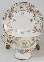 Tea cup and saucer with floral Dresden sprays pattern, gold accents, 3 inch tall cup with footed base, 6 inch saucer diameter, white background with multi-color floral designs