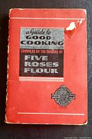Front cover of the red softcover book A Guide to Good Cooking by Five Roses Flour with wear on edges and tear on upper right.