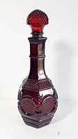 Full view of the ruby red glass decanter with bulbous stopper showing geometric textured panels and hexagonal base.
