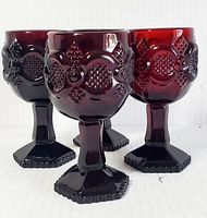 Front angle showing all four deep red glass goblets with textured geometric and floral patterns on bowls and hexagonal bases.