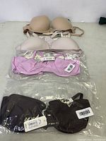 Four bras laid out, two beige, one light pink, one black. Some still in packaging.