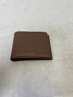 Closed view of the brown COACH leather wallet showing embossed logo on front.