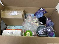 Open box view showing various new baby/kids items including pacifiers, mini cars, and small skincare pots.