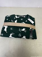 Folded new women's pajama set with tag, green with white reindeer and snowflake pattern, wrapped with beige La Vie en Rose band.