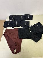 Seven black polka dot panties with three white buttons laid out with one maroon ribbed panty, all medium size and new with tags