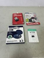 All four items in the lot shown laid out on a surface: Bluetooth USB dongle in package, SanDisk Ultra 32GB microSDHC card with adapter, 60W multifunction data cable set, WYZE 32GB microSD card in package.