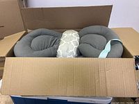 Open box showing padded neck pillows including two grey and one white fabric with floral pattern