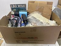 Large cardboard box filled with various crafting and miscellaneous items including permiting view of heat tool and tubes