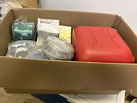 Box containing various miscellaneous items including a red plastic case, wrapped filter material, white Yamaha parts box, and coiled flexible metal conduit.