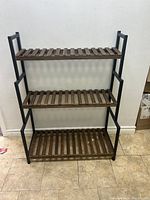Full view of the three-tier plant stand/shelf showcasing black metal frame and wooden slats.