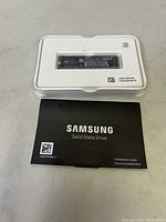 Samsung 970 EVO Plus 1TB SSD in protective plastic packaging on white insert with installation and warranty booklet below.