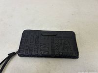 Black Steve Madden wallet side view showing embossed repeating brand name pattern