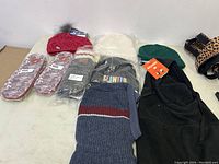 Overview of winter accessories laid out on table including knit hats in red, white, green, and blue, gloves, and insoles. Some still in plastic packaging.
