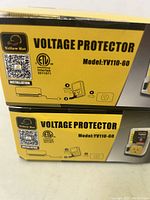 Two boxed Yellow Hat voltage protectors model YV110-60 stacked, showing product name, model number, and basic usage illustration on the side of the box.