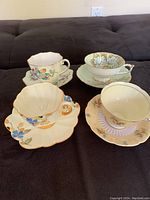 Four Paragon porcelain teacups and saucers displayed on dark surface showing colorful floral prints and scalloped rims.