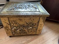 Wooden box with brass high relief side panel showing people and a building scene, highlighting thickness and patina of the wood and brass.
