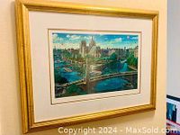 Front view of framed serilithograph showing colorful depiction of Notre Dame and river with bridges under blue sky.