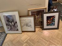 Four framed artworks leaning against a wall, including an Inuit print, a misty tree watercolor, and two other framed pieces.