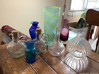 Overview of glass vases displayed on table including aqua green spiral vase, cobalt blue vase, clear and purple vases
