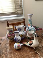 Five hand painted ceramics including vases, pitcher, and decorative bird on a wooden table with natural light.