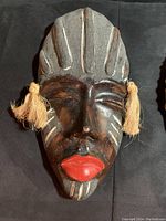 Front view of the handcrafted ceramic mask showing facial features, colors, and tassels.